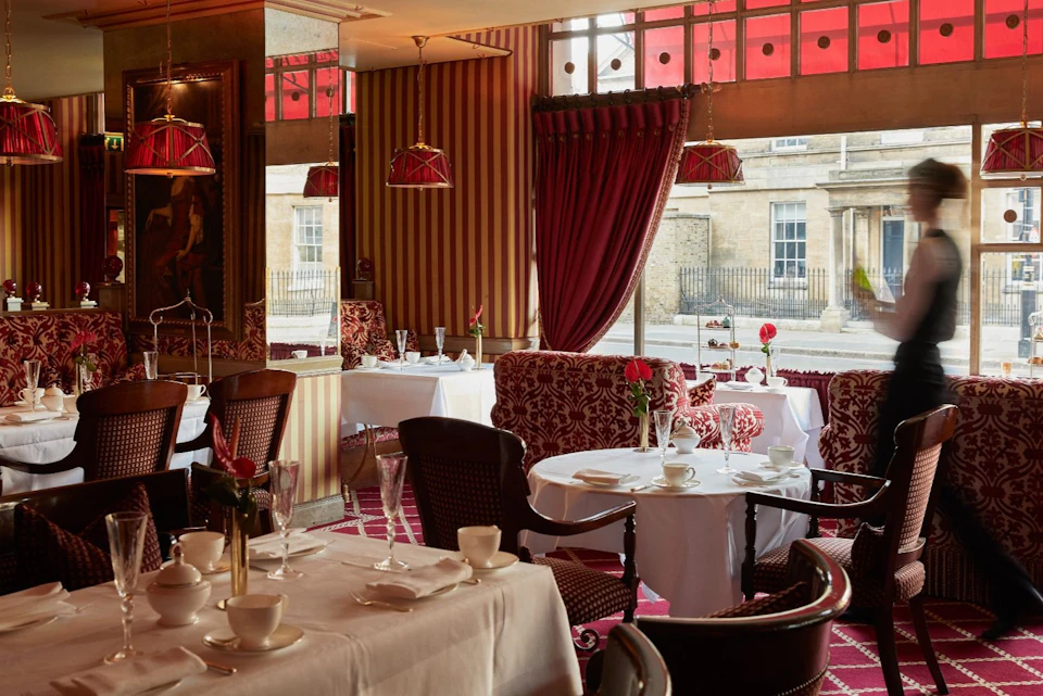 Elegant restaurant interior with red and gold decor, white tablecloths, and windows overlooking a street.