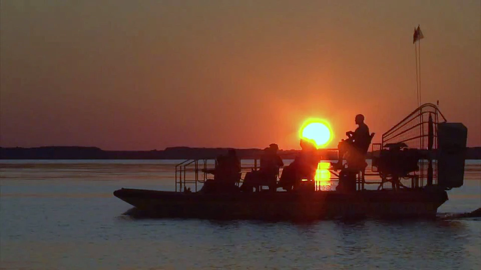 Silhouetted people on a boat against a sunset over a calm body of water.