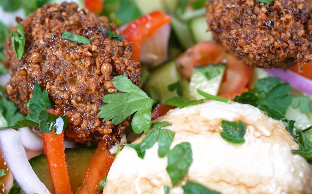 Close-up of a plate with falafel, hummus, sliced cucumber, tomato, and parsley garnished with herbs.