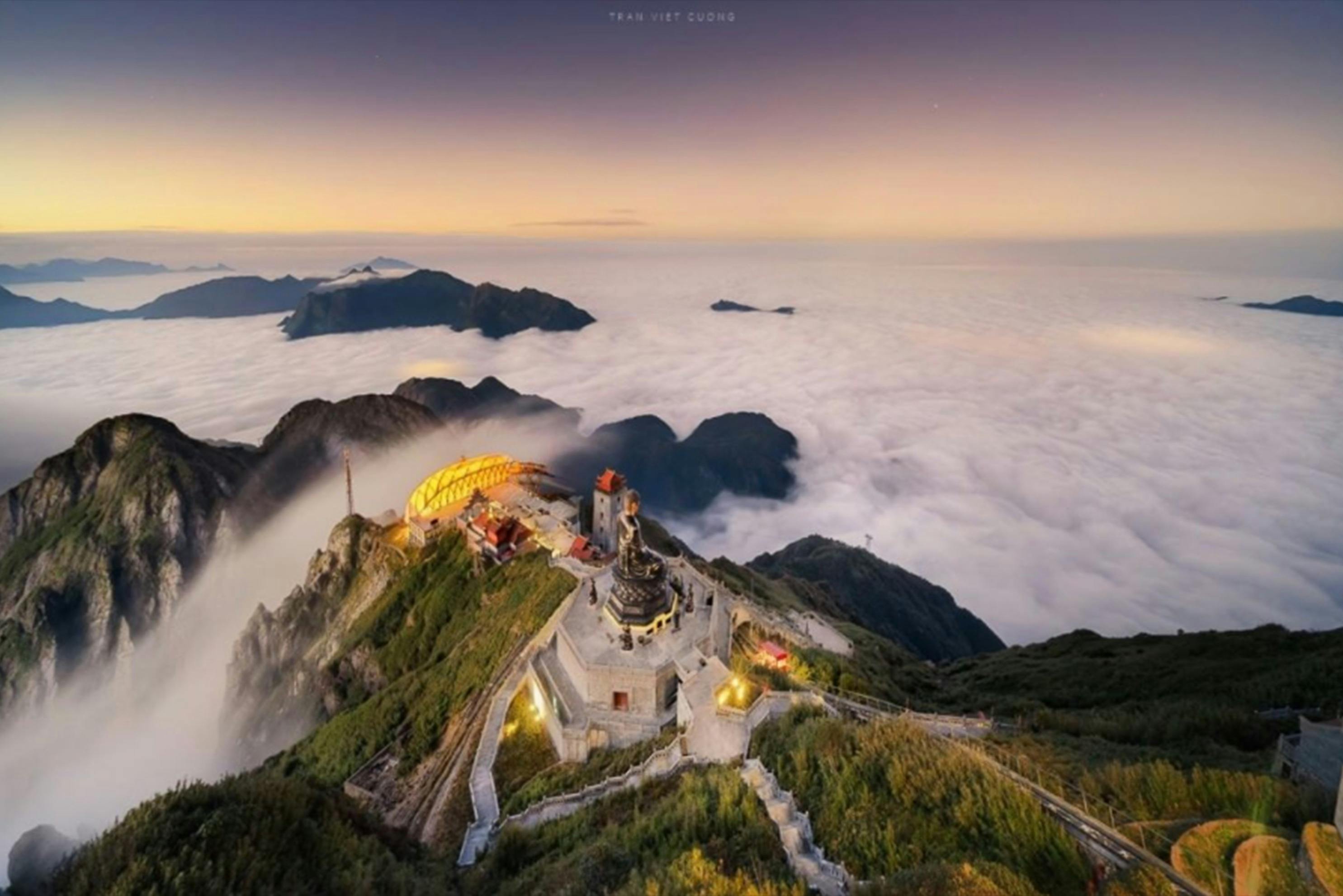 커다란 동상과 화려한 건물, 노을이 질 무렵 구름 위로 빛나는 다리가 있는 산꼭대기의 공중 전망.