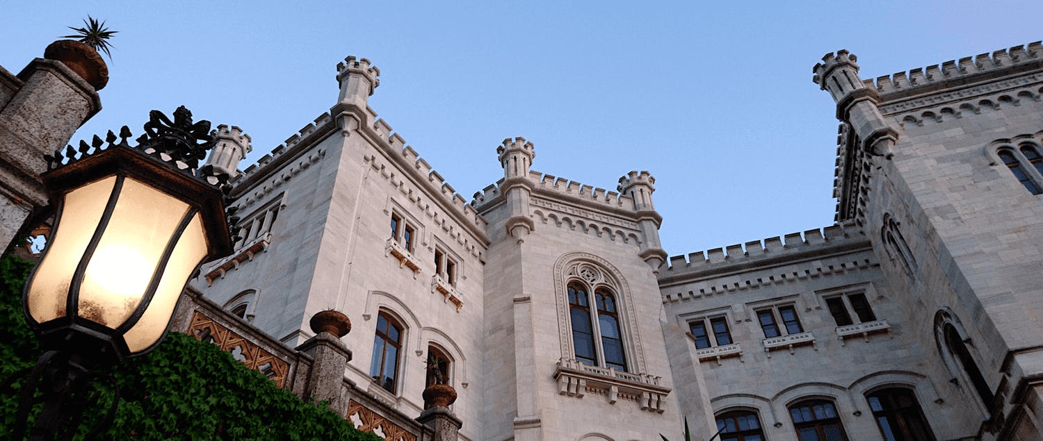 Stone castle facade with arched windows and decorative towers against a clear blue sky.