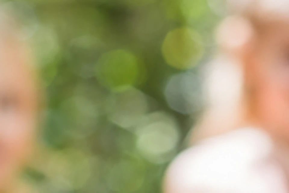 Two young girls in matching pink dresses are being photographed in a forest setting. The focus is on the smartphone taking the photo.
