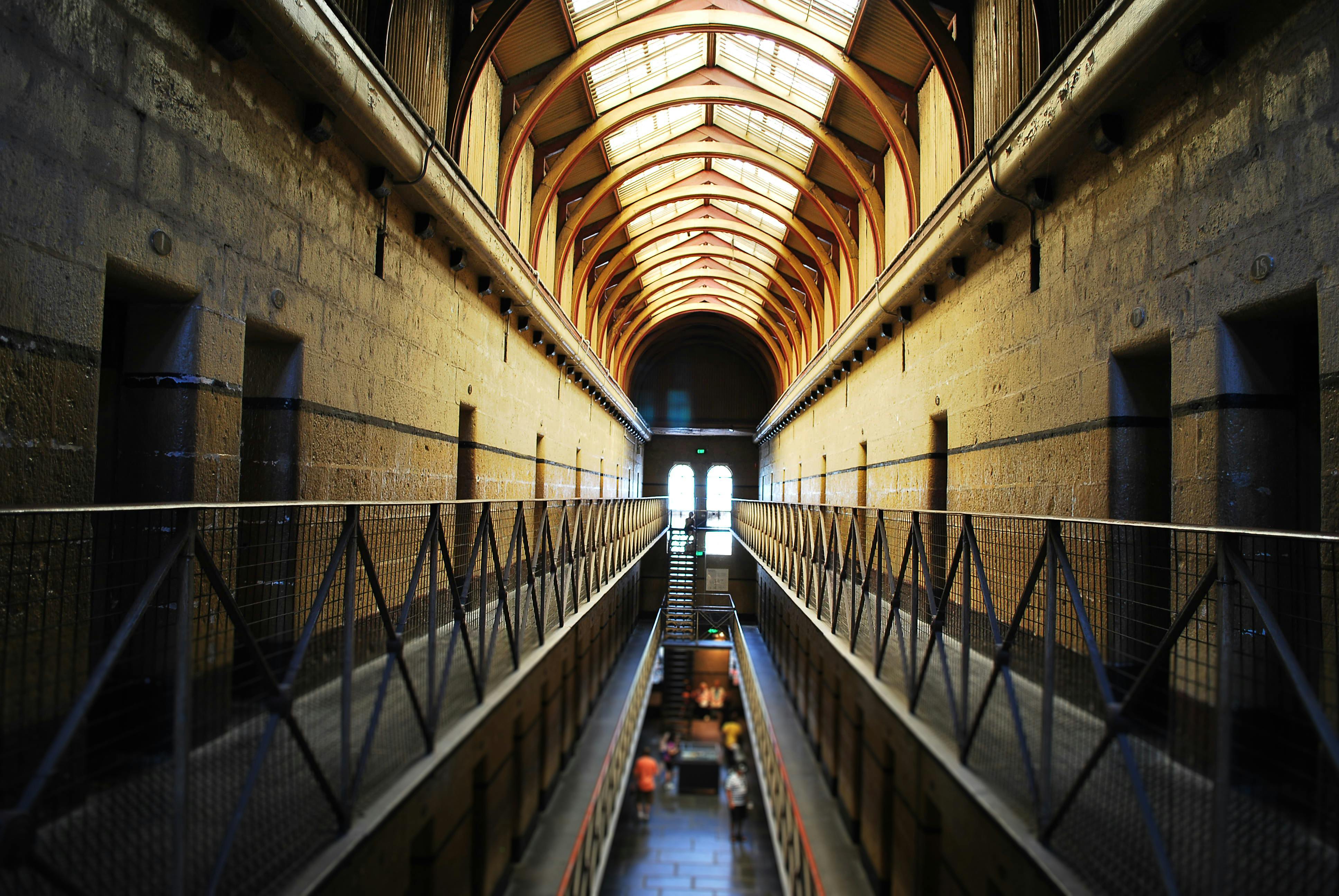 Interior corridor of a historical building with high arched ceiling, metal railings, and a symmetrical layout, leading to a bright window.