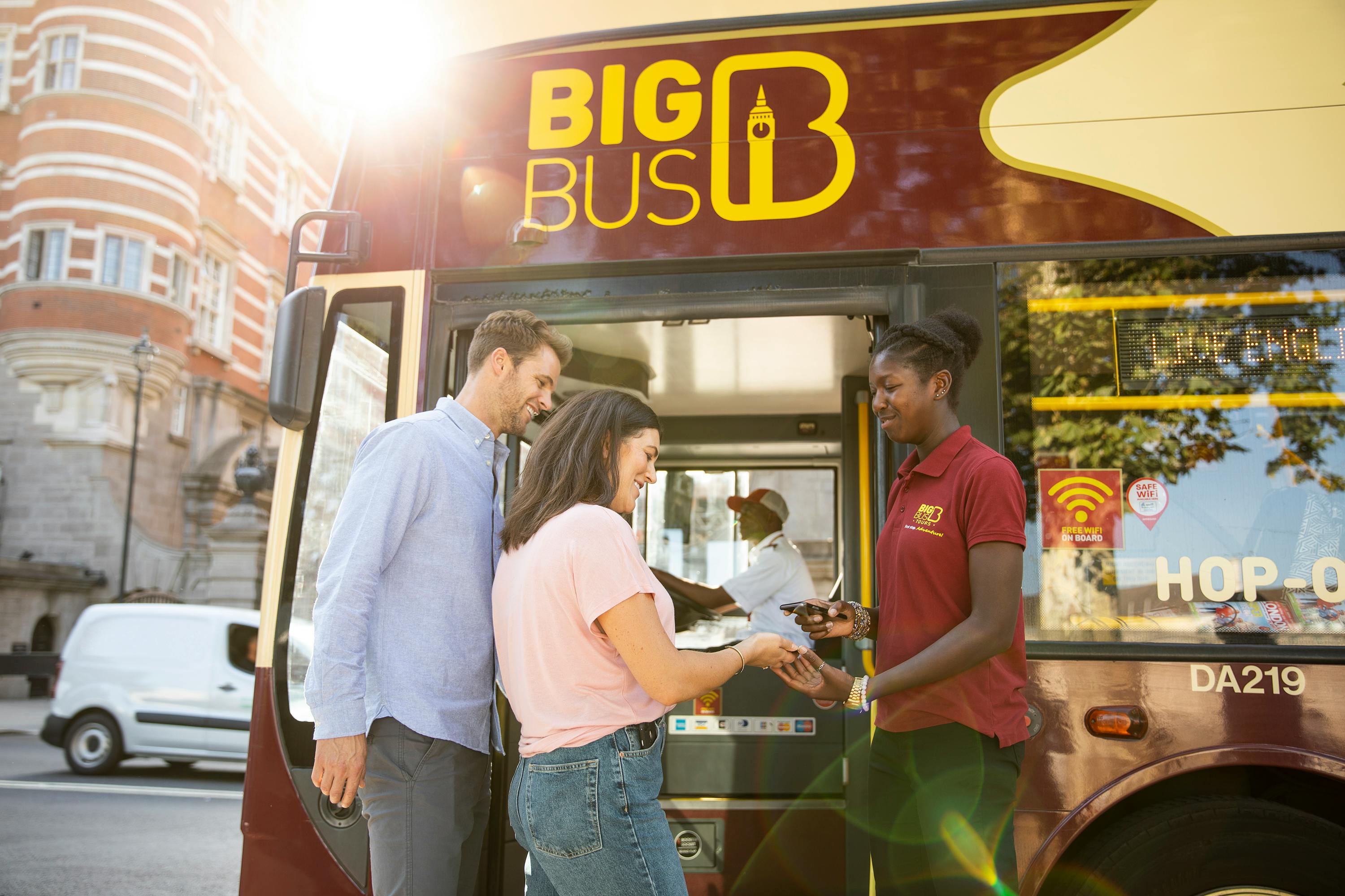 Una coppia compra i biglietti da un addetto all’ingresso di un autobus turistico “Big Bus” color granata.