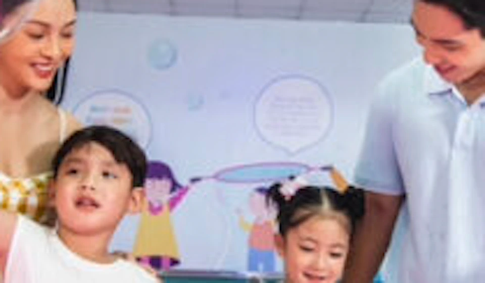 A family of four is playing with large soap bubbles in an indoor activity center with colorful lighting.