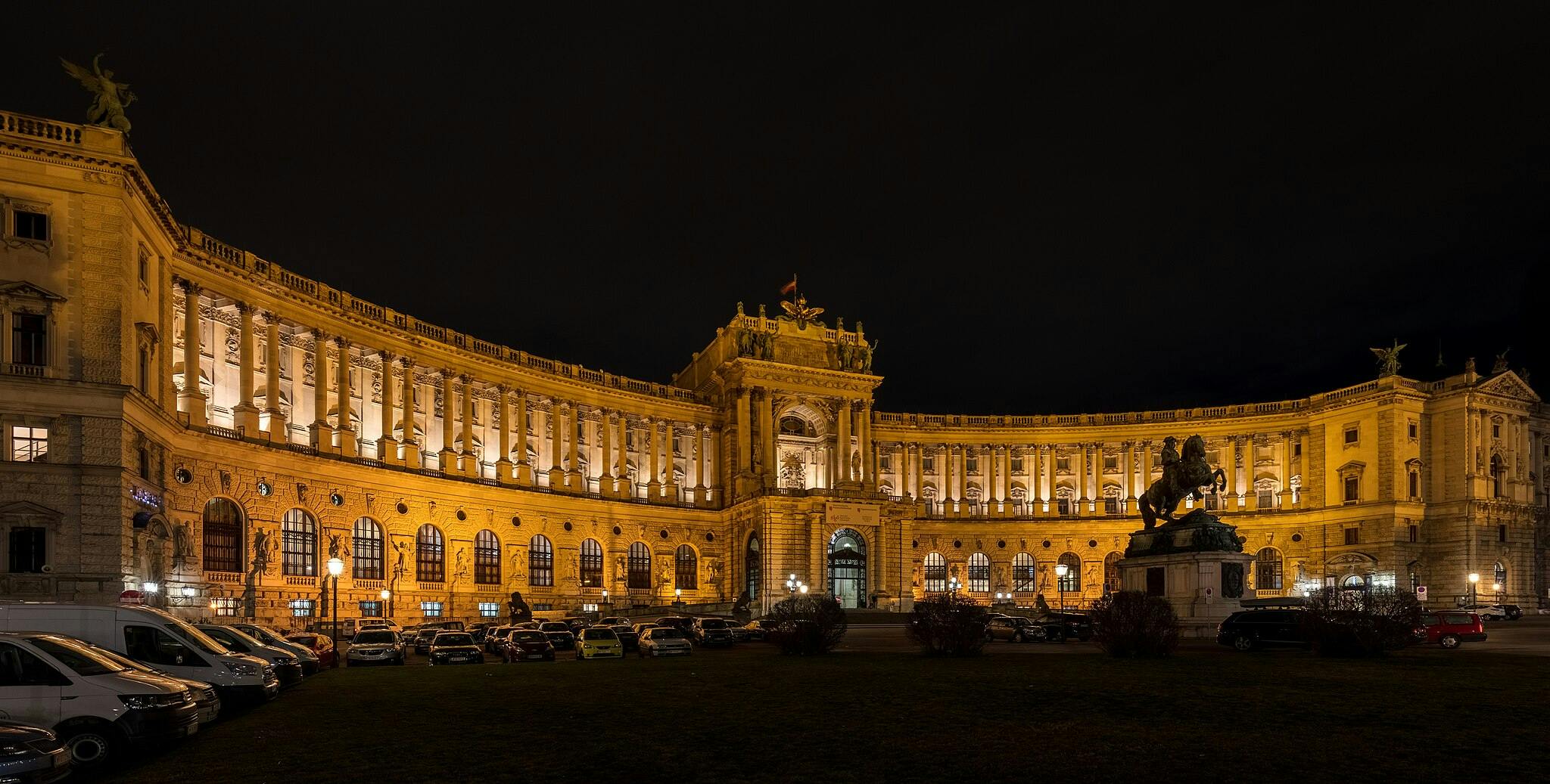 Bâtiment historique éclairé de nuit avec une arcade centrale, des colonnes et une statue de cheval au premier plan.