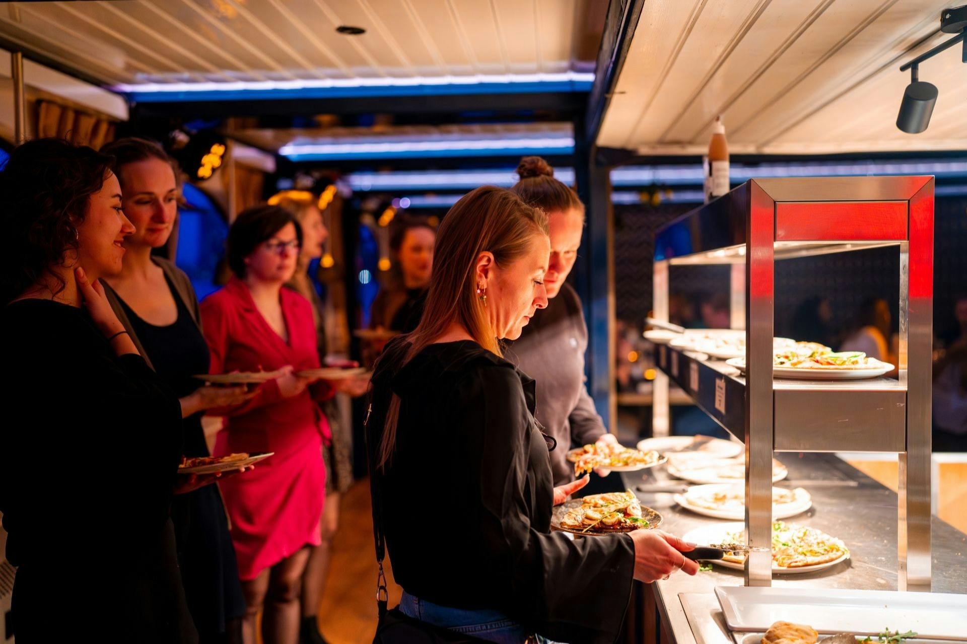 Människor väljer mat från en buffélinje i en väl upplyst inomhusmiljö med fokus på en person som serverar sig själv.