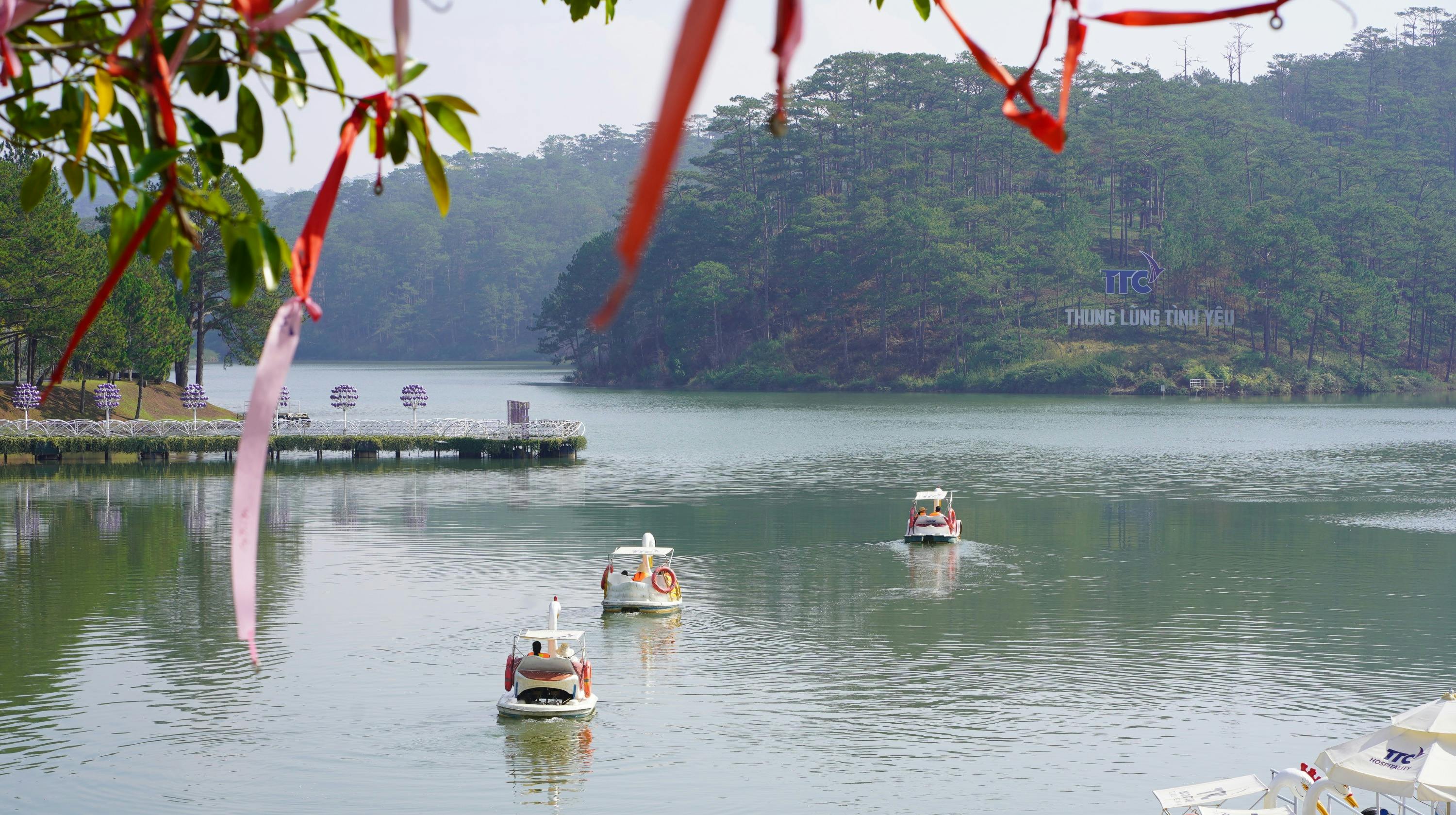 Pedal boats shaped like swans on a calm lake surrounded by forested hills under a hazy sky.