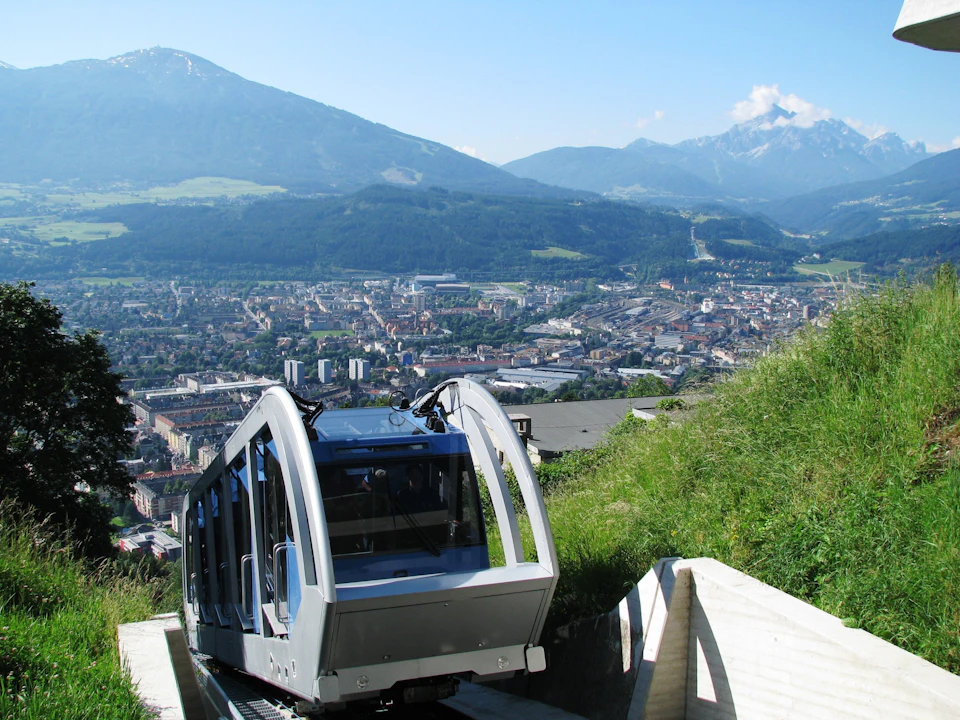 A funicular railway car ascending a steep hill with a city and mountainous landscape in the background.