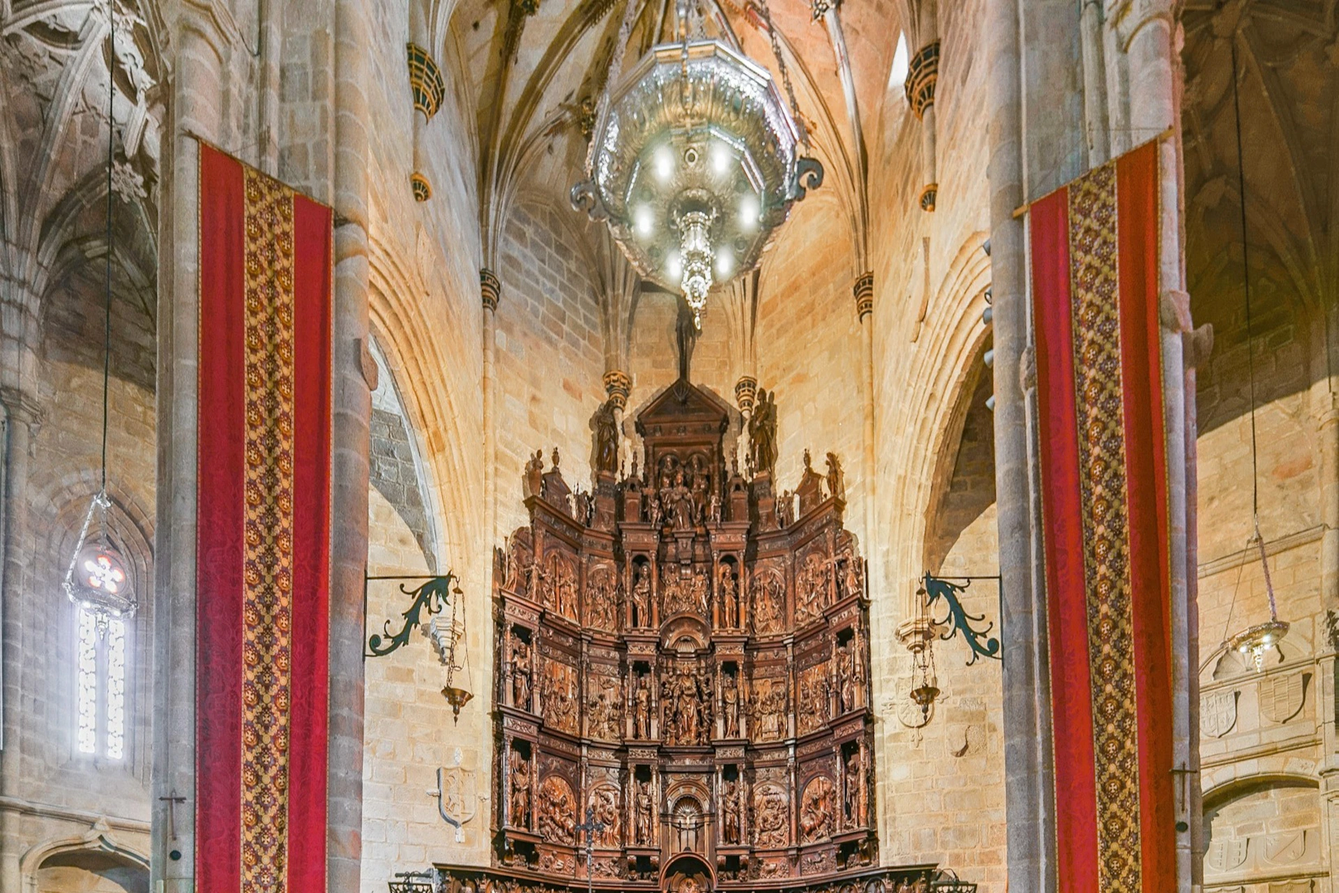 Ornate wooden altar with intricate carvings in a cathedral interior, featuring tall stone arches and a large chandelier above.