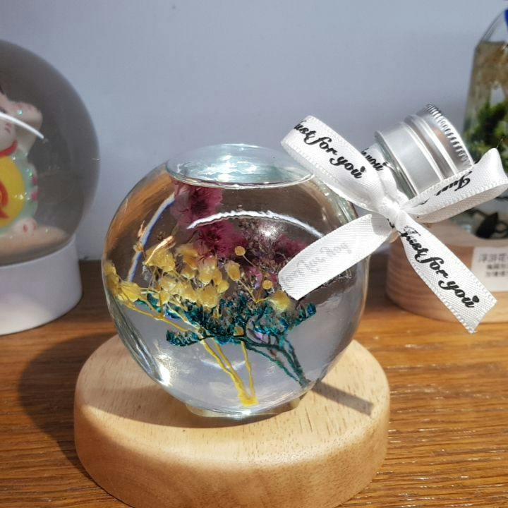 A clear glass sphere containing preserved flowers, tied with a ribbon, displayed on a wooden stand.