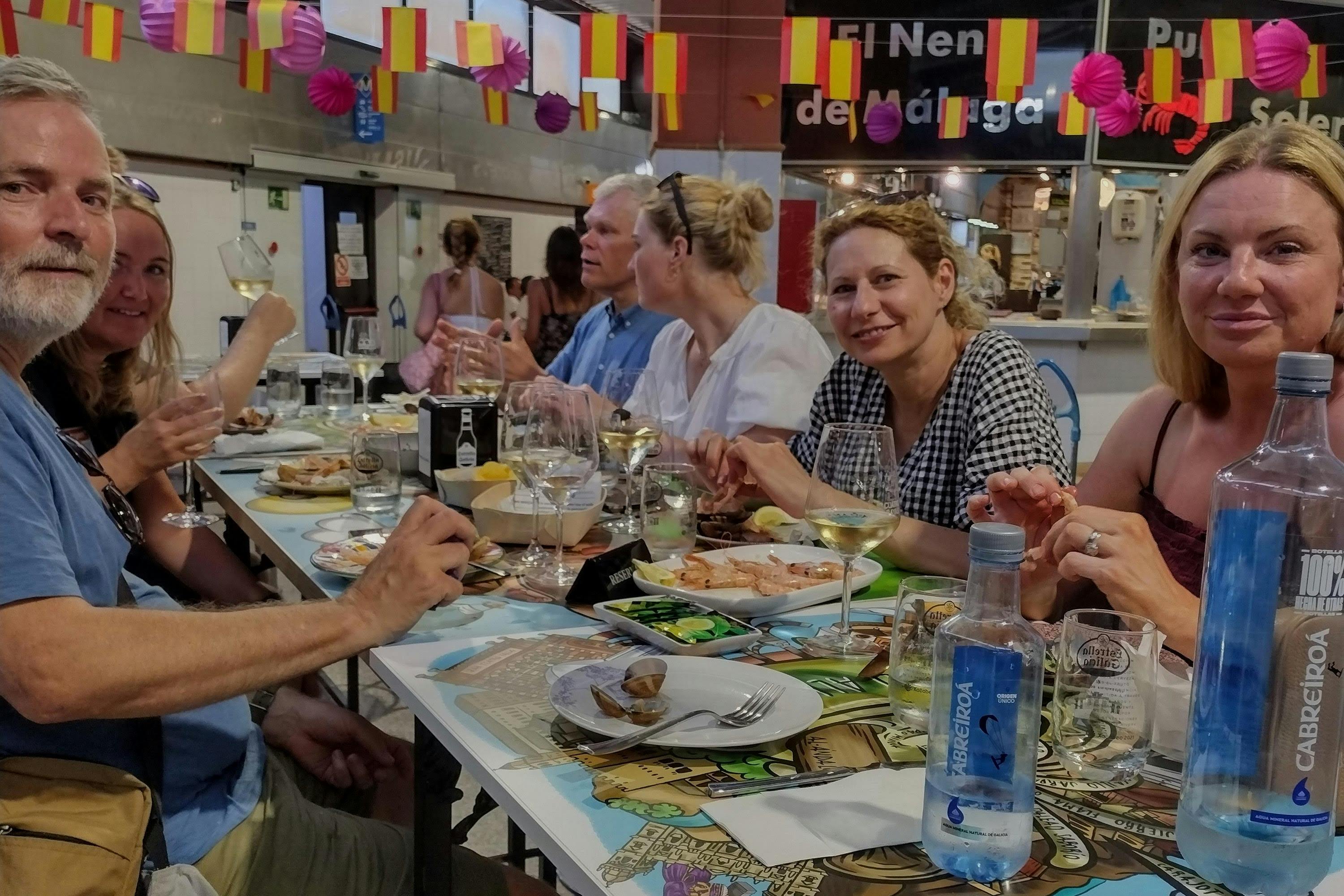 Un groupe de personnes prend un repas dans un lieu intérieur décoré, partageant des boissons et de la nourriture autour d'une longue table.