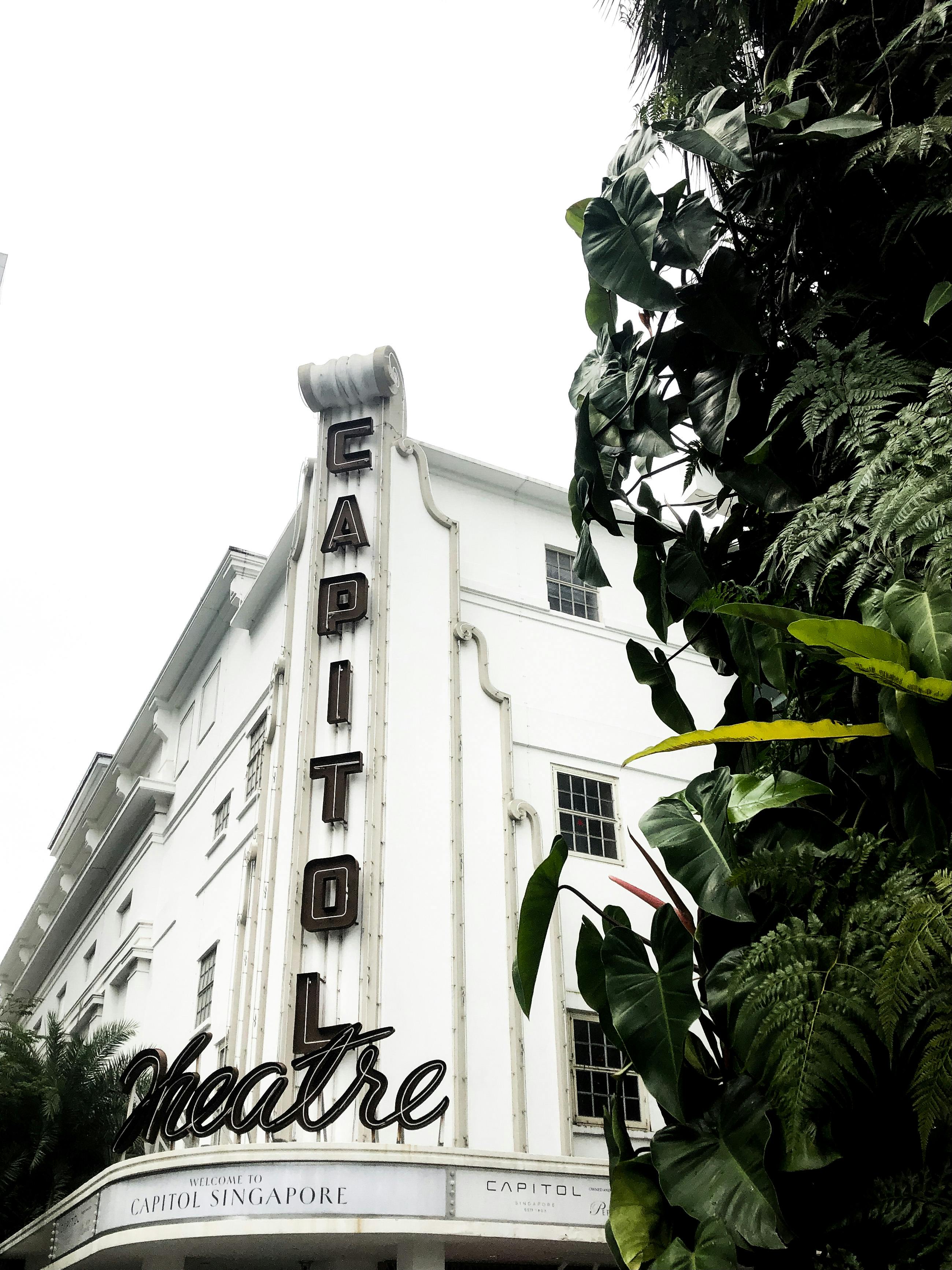 Un edificio bianco con una scritta verticale "CAPITOL" accanto a del verde e alla parola "Theatre" in corsivo.