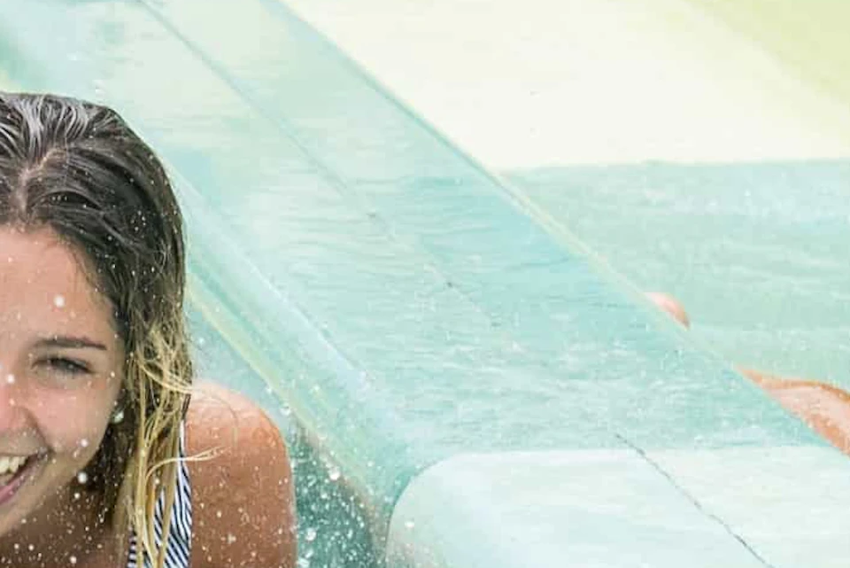 Three people slide down parallel water slides on mats, smiling and surrounded by lush greenery.