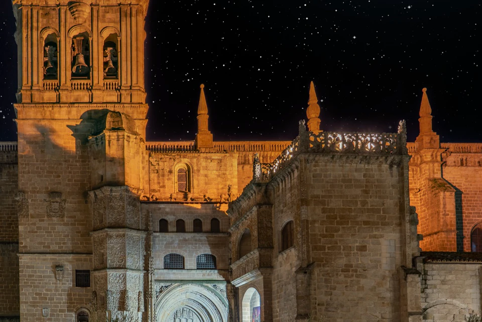 Illuminated stone cathedral at night with a starry sky in the background.