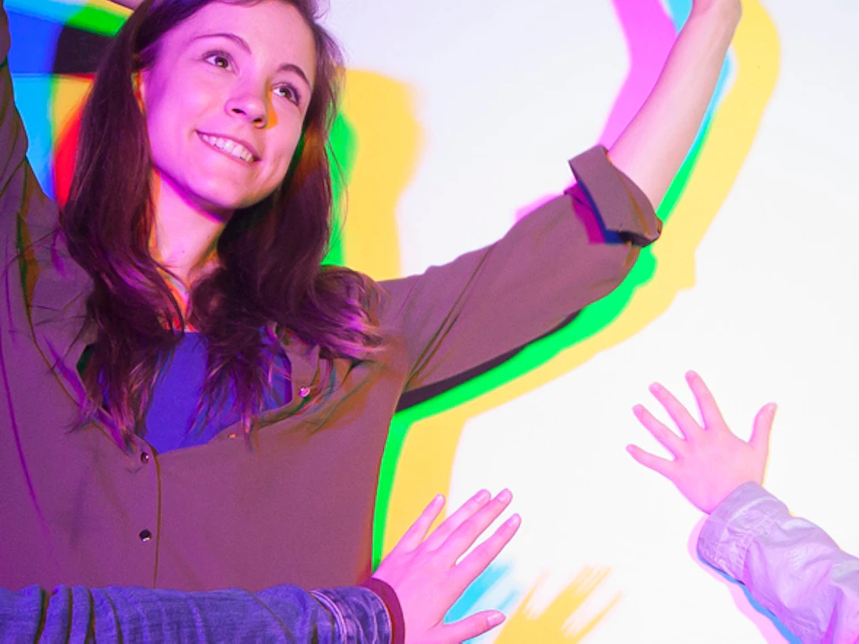 Four people strike playful poses against a wall with colorful shadows cast by multi-colored lights.