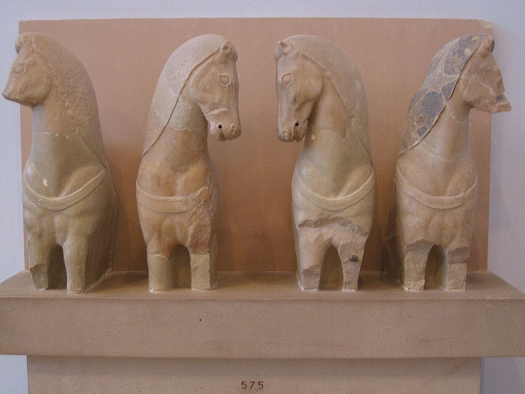 Ряд из четырех древних каменных скульптур лошадей, выставленных на бежевой полке.