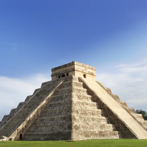 Eine uralte Steinpyramide mit steilen Stufen unter einem strahlend blauen Himmel, umgeben von Grün.