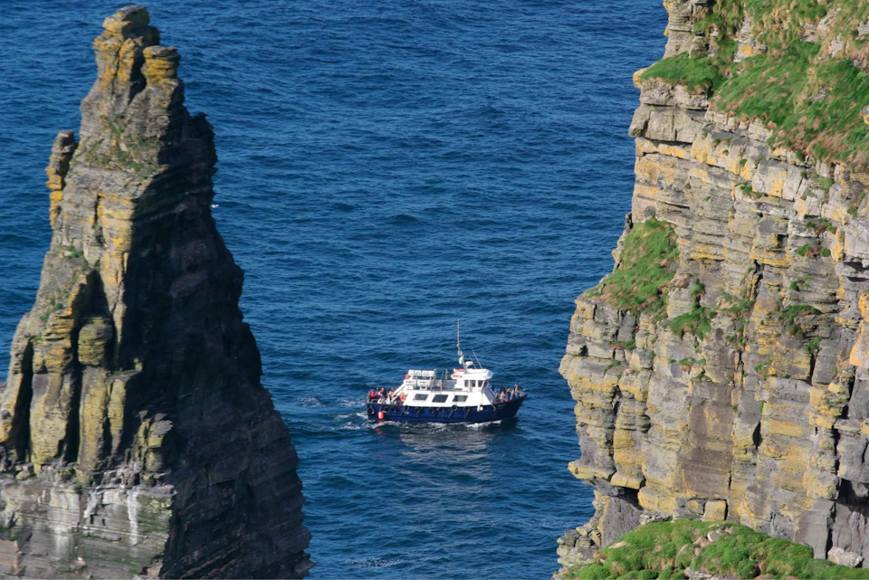 A white and blue boat sailing between two towering cliffs over a calm blue sea.