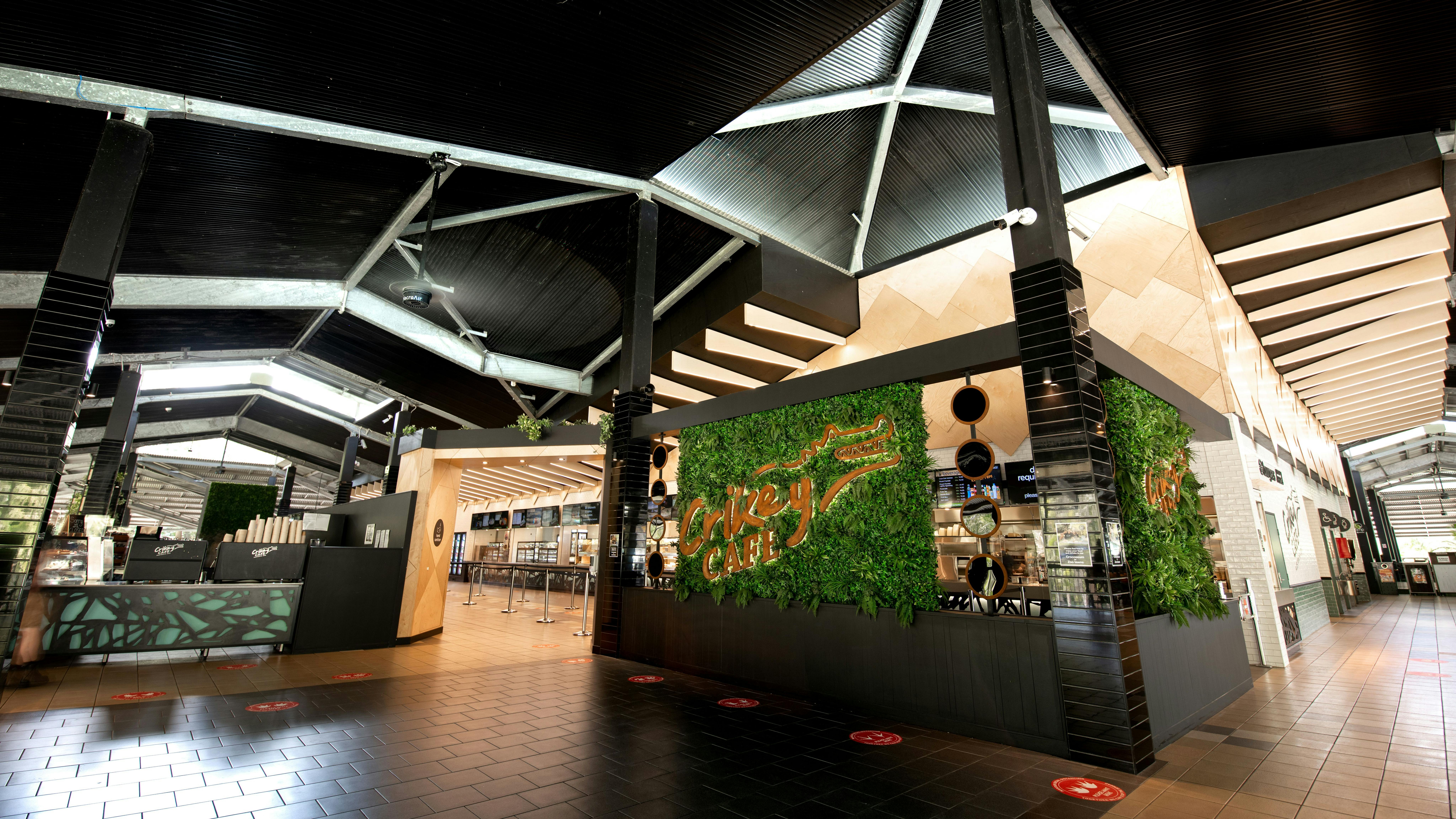 黒とメタリックなアクセントの広々としたエリアにある、「コーヒーカフェ」と書かれた緑色の緑豊かな看板が付いたモダンなカフェ。