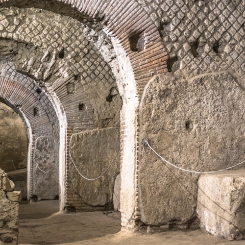 Ancient stone and brick arched passageway with Roman-style design, featuring textured walls and enclosed by ropes.