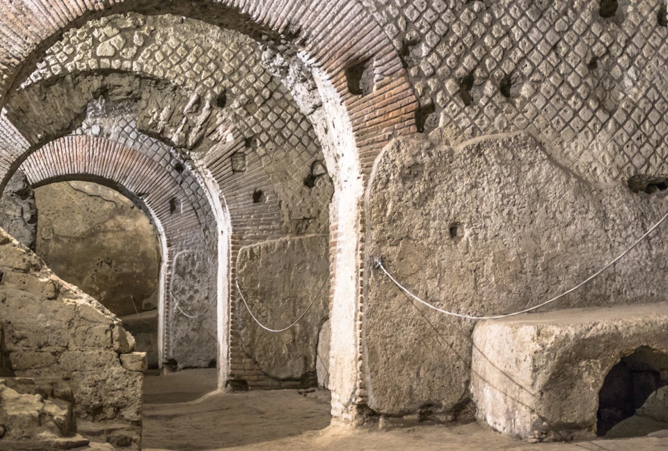 Ancient stone and brick arched passageway with Roman-style design, featuring textured walls and enclosed by ropes.