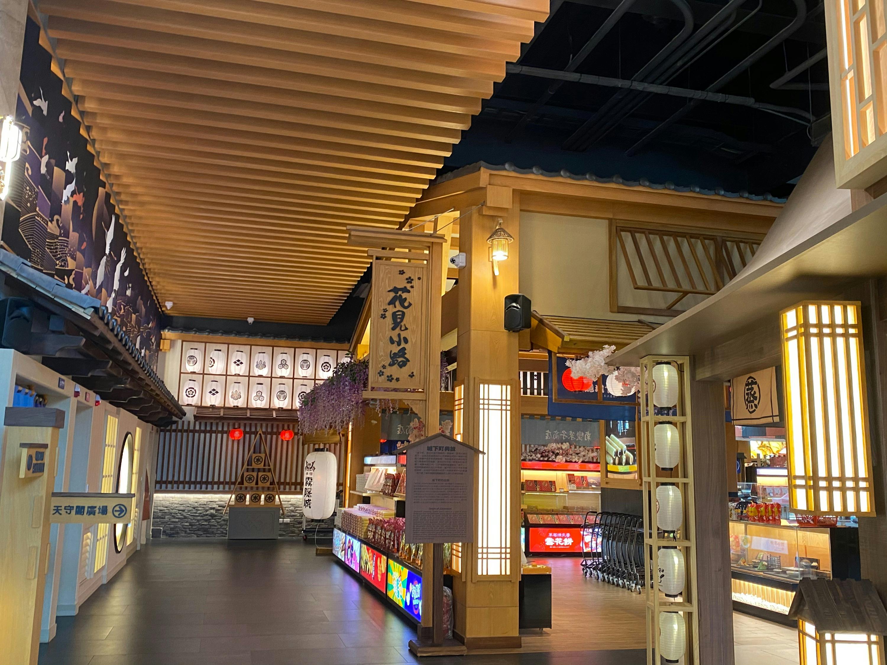 A brightly lit indoor market styled with traditional Japanese architecture, featuring wooden details and lantern decorations.