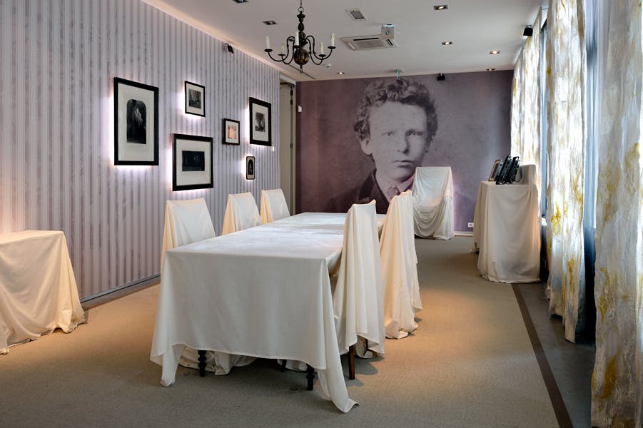 Δωμάτιο με τραπέζια και καρέκλες καλυμμένα με λευκό ύφασμα, μεγάλο vintage πορτρέτο στον τοίχο, κορνιζαρισμένες εικόνες, πολυέλαιο και κουρτίνες.