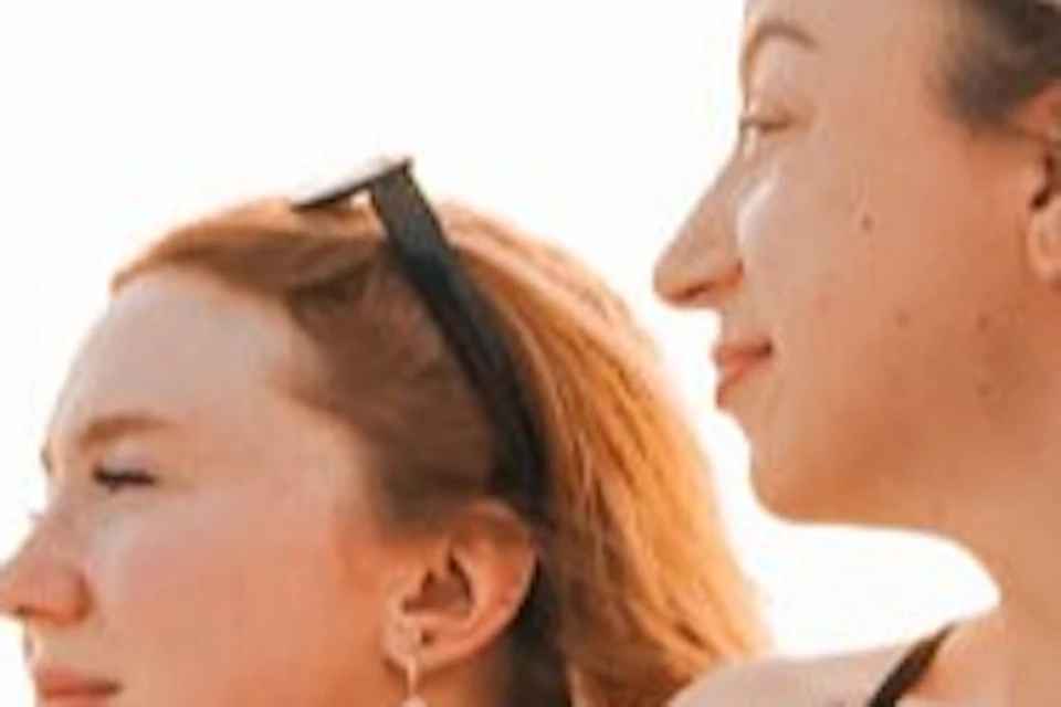 Two women sit on a white yacht deck under a clear sky, with part of the yacht's name visible in red letters.