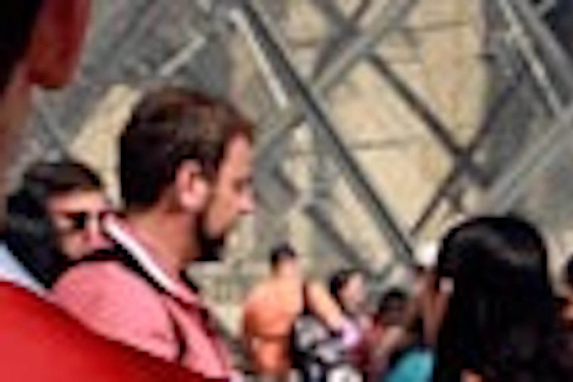 A woman on a bicycle speaks to a person wearing a red vest with 'Paris City Vision' in front of the Louvre Pyramid.