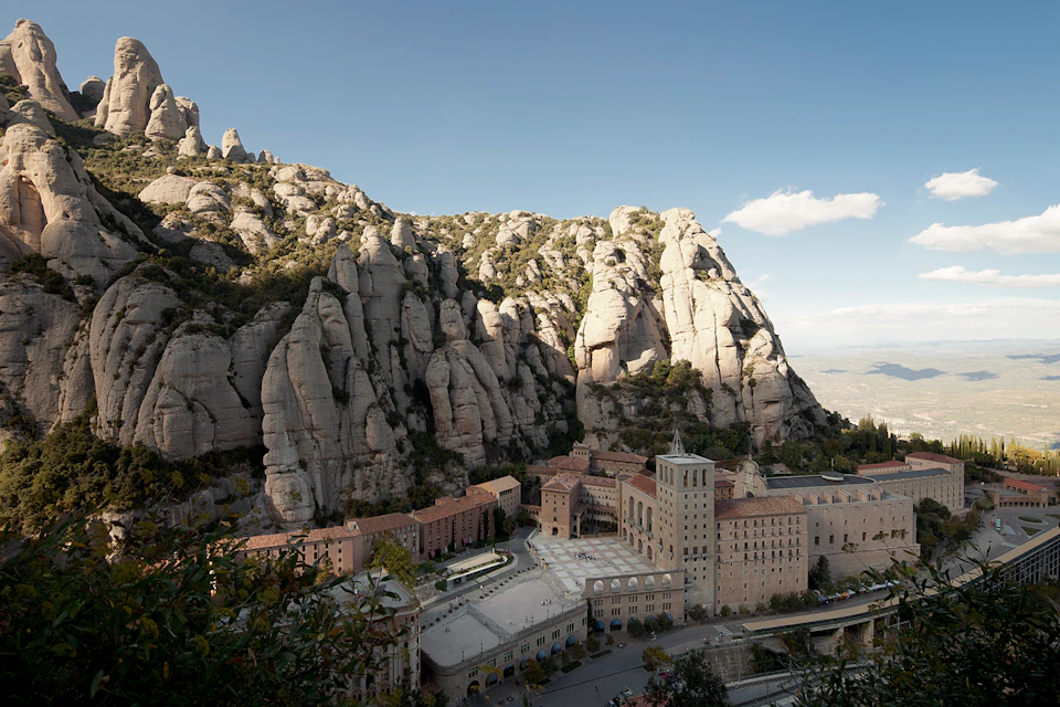 A stone monastery complex nestled against large, rugged rock formations with a clear sky in the background.