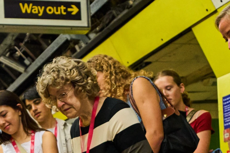 A group of people observes a boy on a subway platform who is interacting with a small object on the ground.