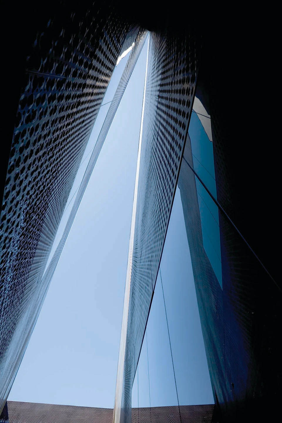 Tall, modern, reflective buildings with a narrow gap between, showing the sky above.