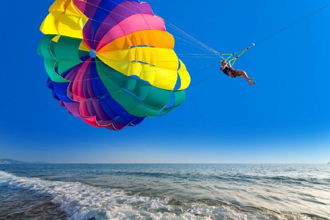 Person parasailing with a colorful parachute over the ocean on a clear, sunny day.