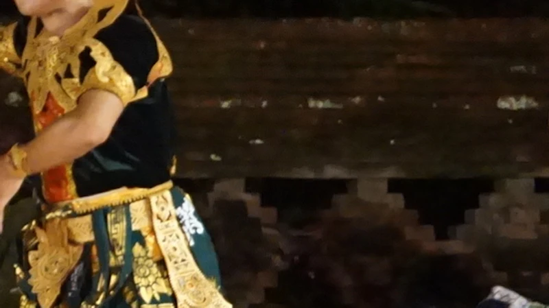 Traditional dancers in ornate costumes perform on a stage with musicians and a temple-like backdrop in the evening.