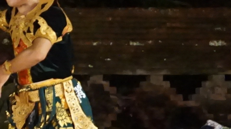 Traditional dancers in ornate costumes perform on a stage with musicians and a temple-like backdrop in the evening.