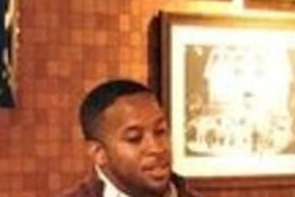 A man in a vest talks to three guests, including a child; they are in a warmly lit, framed photo-decorated lounge.