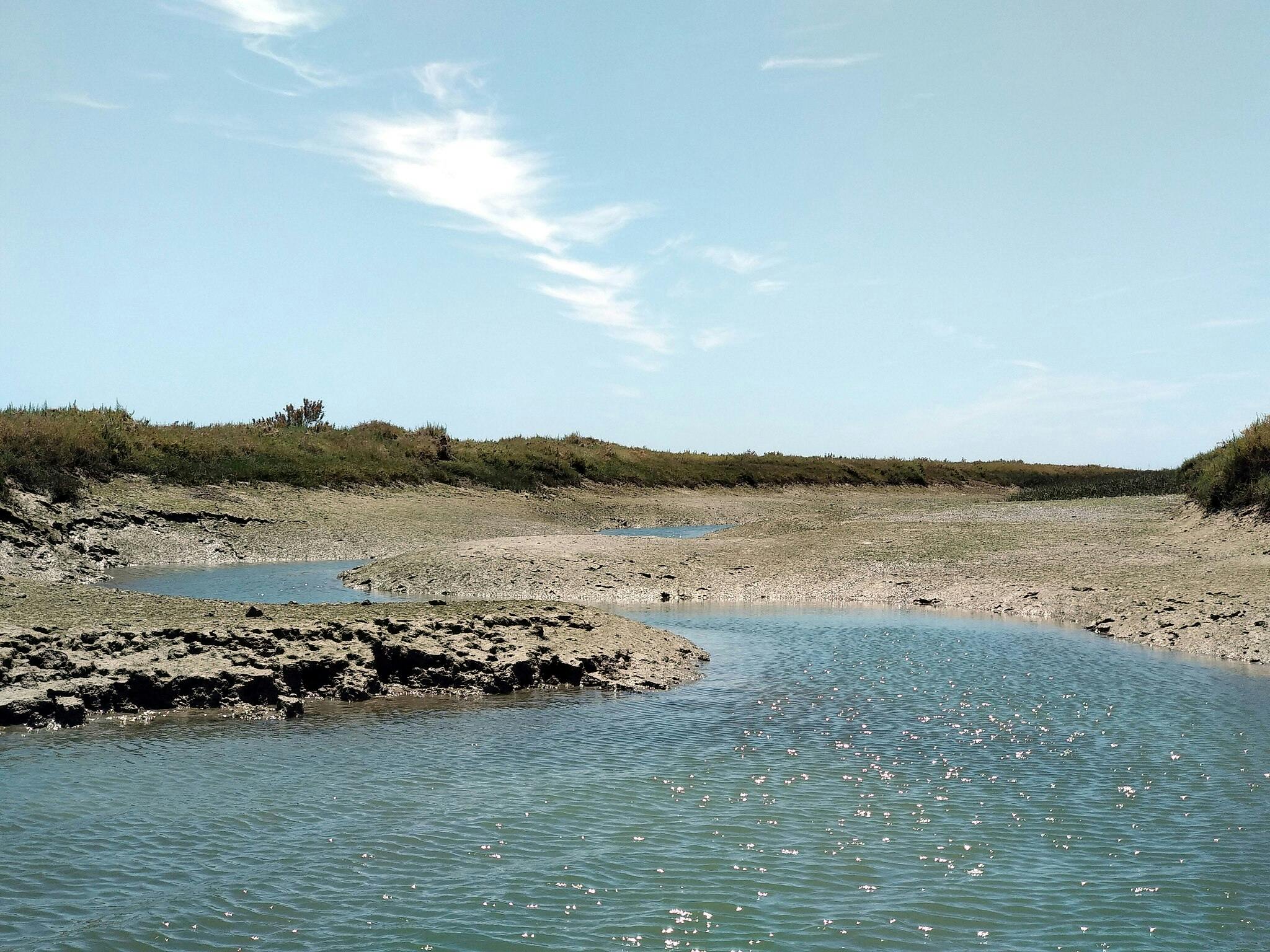 在一片多云的天空下，一条浅而蜿蜒的溪流清澈的蓝色水流穿过干燥的岩石景观。