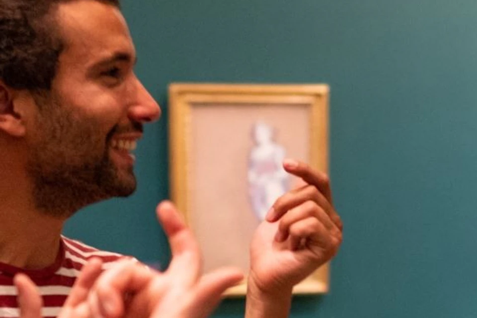 Three people conversing in an art gallery, with paintings on the walls and a teal background.