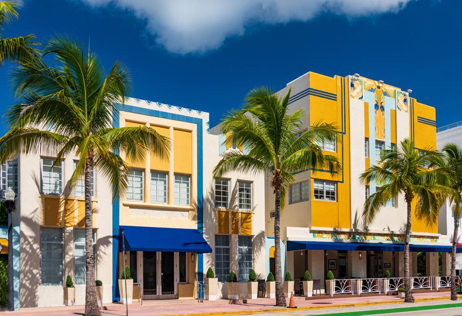 Colorful Art Deco buildings with blue awnings and palm trees under a clear, blue sky.
