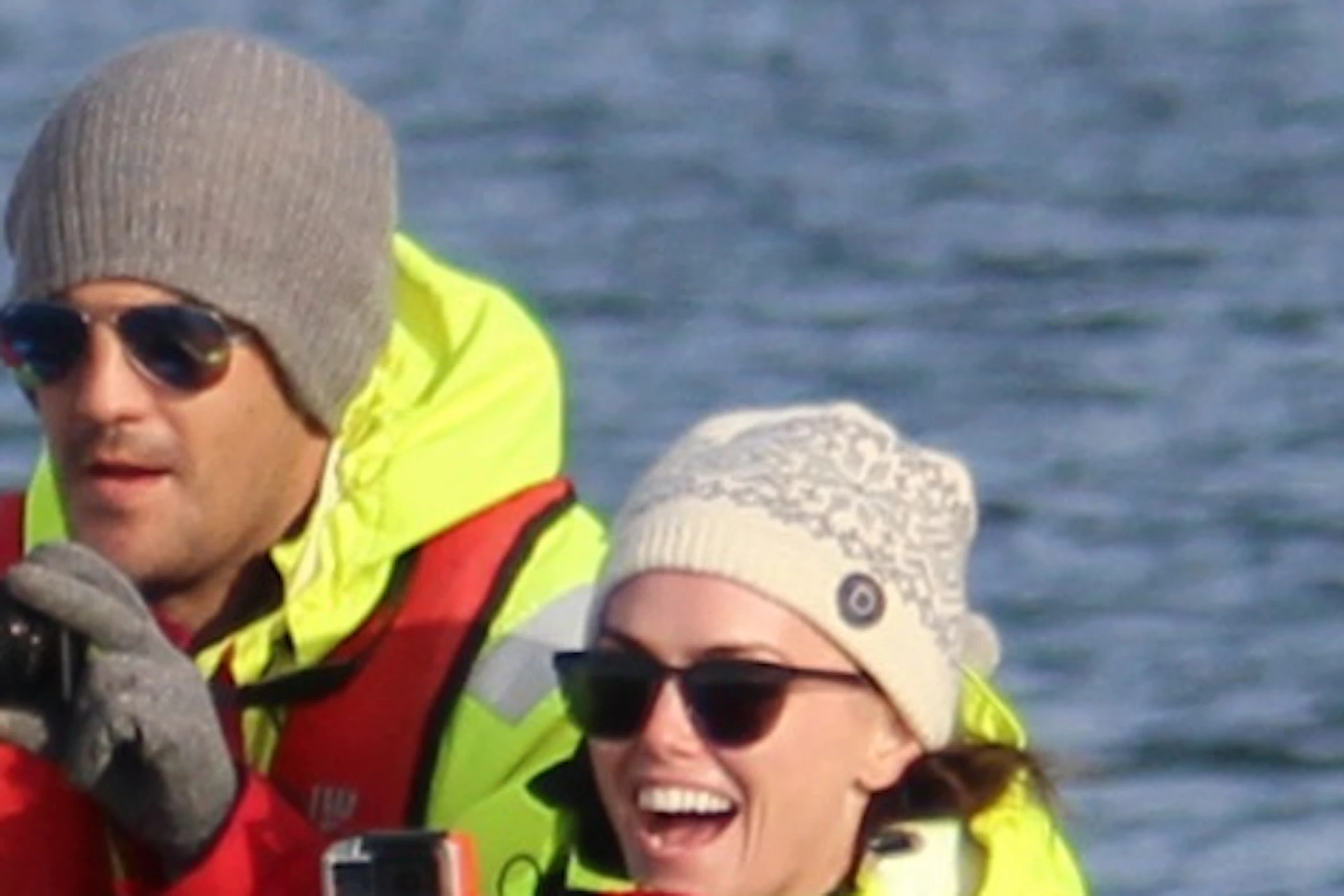 A group of people in red outerwear on a boat taking photos of a whale's tail emerging from the water.