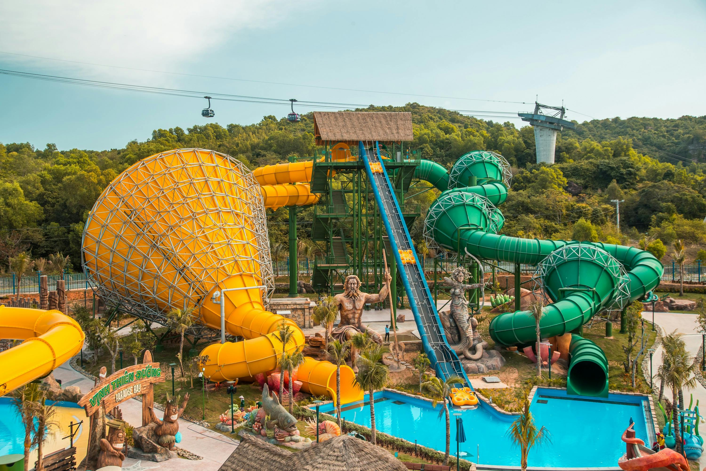 A colorful water park with large yellow and green slides, a pool, and a lush green landscape in the background.