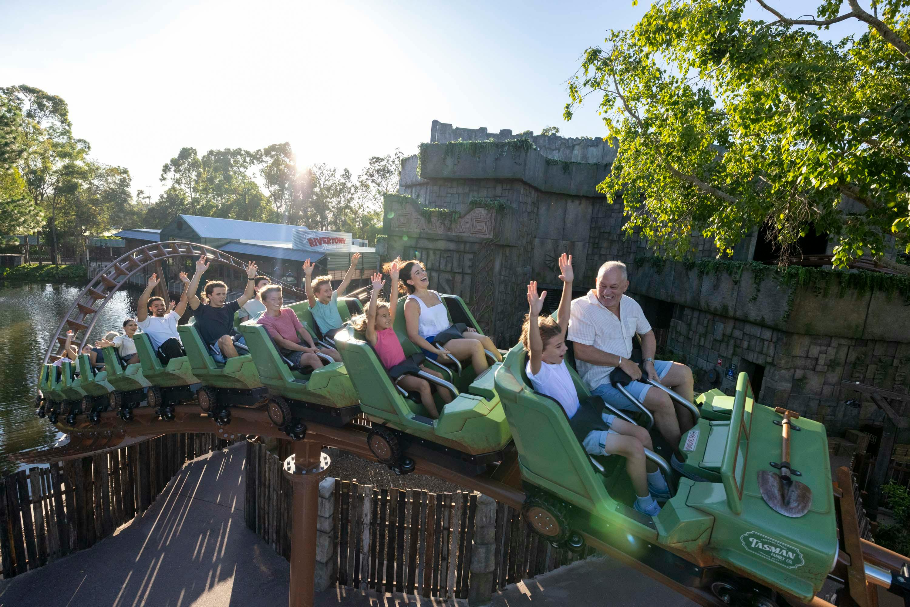 A group of people enjoying a jungle-themed roller coaster ride in green cars on a sunny day.