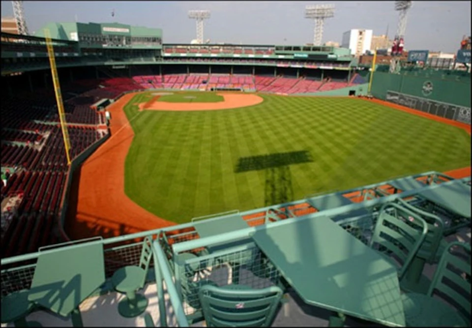 Empty baseball stadium with green seating area in the foreground and well-manicured grass field with dirt infield beyond.