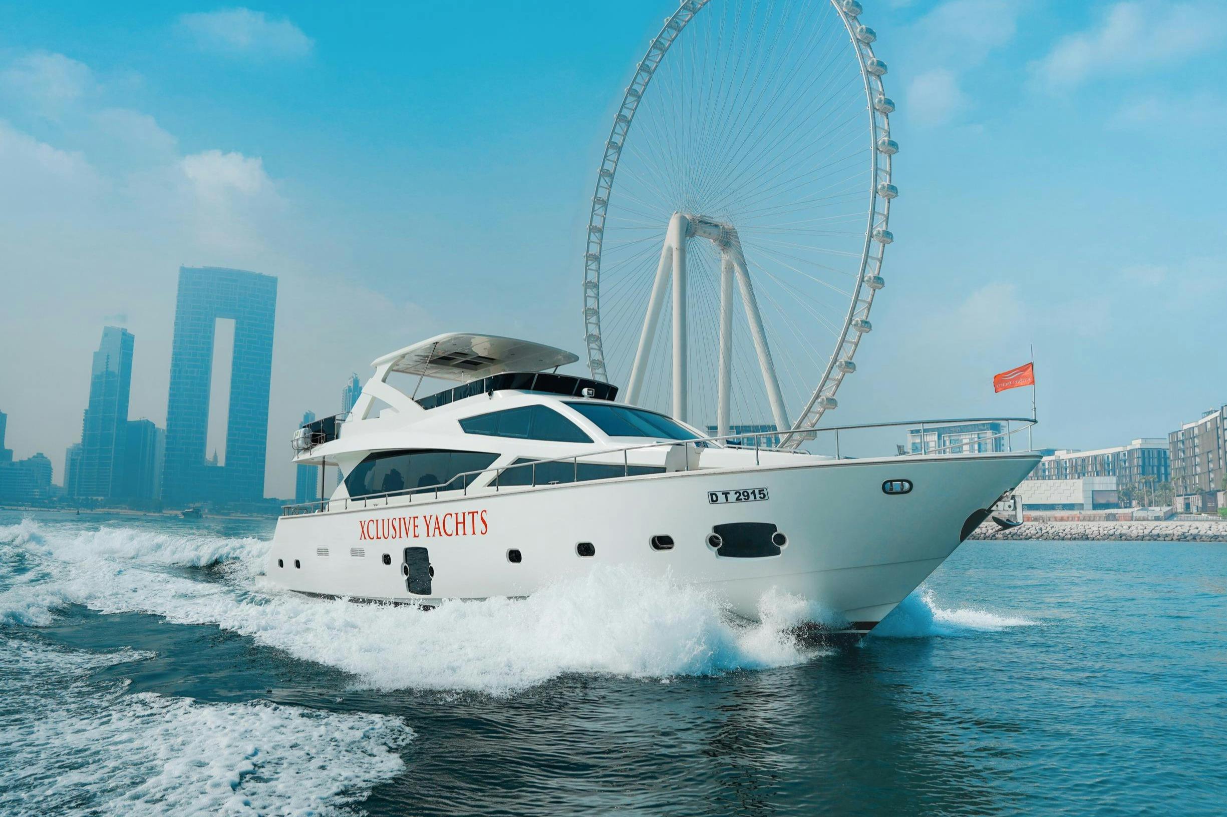 Bílá jachta s názvem „Xclusive Yachts“ na boku pluje na vodě s velkým ruským kolem a mrakodrapy v pozadí.