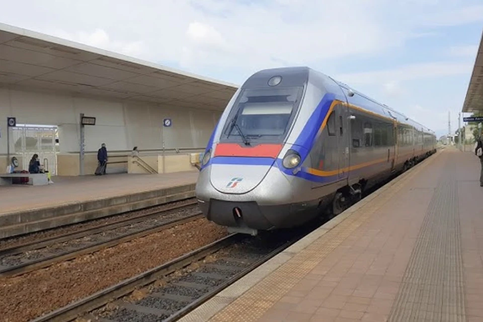 A modern train stopped at a clean, empty platform with a person standing alone near a station building.