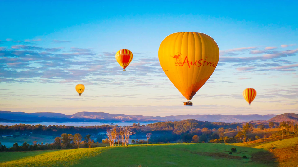 A hot air balloon floats above a misty landscape with trees at sunrise.