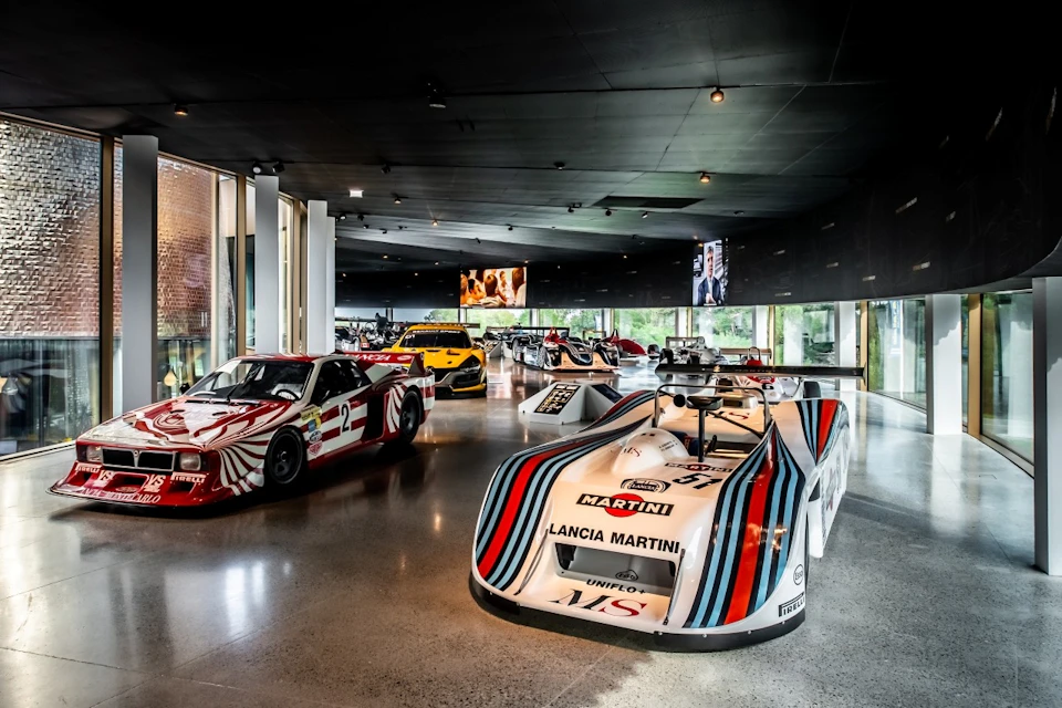A sleek automotive showroom displaying several vintage race cars under soft lighting, including a prominently featured Lancia Martini.