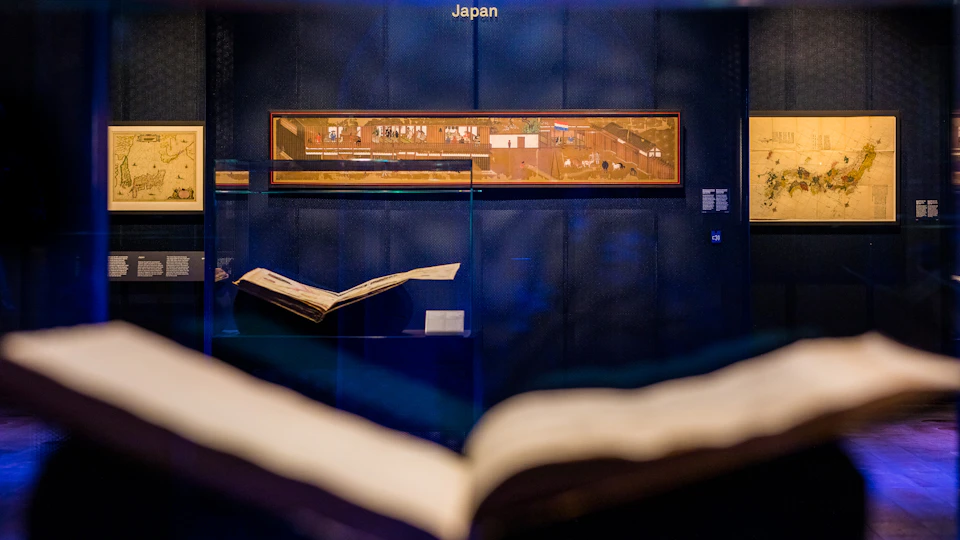 Museum exhibit showcasing a Japanese scroll painting on a dark blue wall with two open books displayed in the foreground.