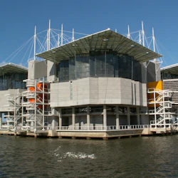 En modern byggnad med kantiga tak och livfulla orange och gula accenter över vatten, under en klarblå himmel.